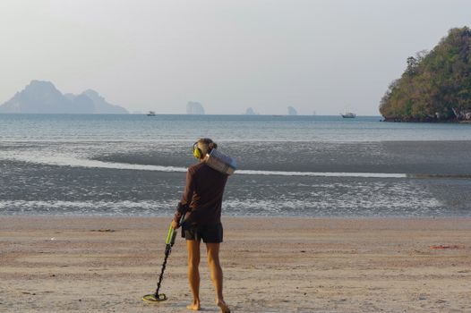 a treasure hunter with Metal detector on sunrise on the beach