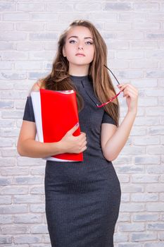 Young beautiful girl model with long hair imitates business lady, office manager or administrator with red folder of documents