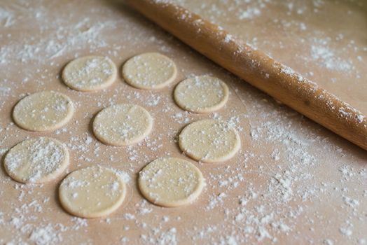 The dough rolled with circles and rolling pin for made ravioli on a wooden table