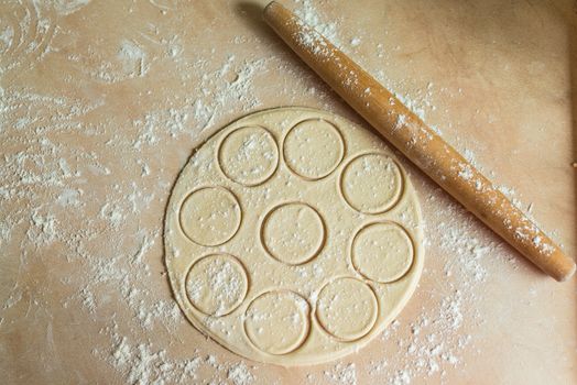 The dough rolled with circles and rolling pin for made ravioli on a wooden table