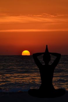 Silhouette of young woman practicing yoga on the beach at sunrise