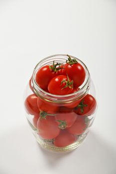 Glass jar full of red cherry tomatoes ready to pickle for conservation over white background, high angle view