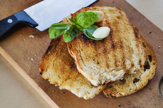Three roasted slices of bread with garlic, fresh basil and a knife on the side.