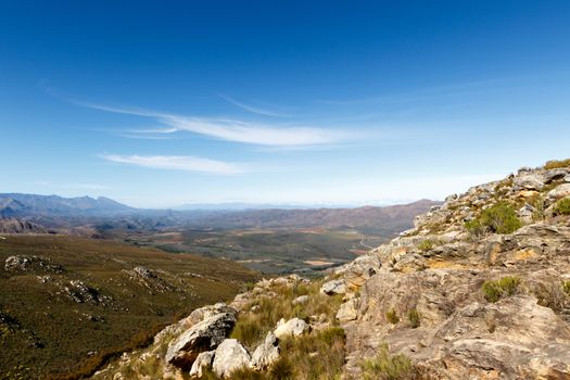 In the middle of The Swartberg Pass looking down at a green valley surrounded by mountains