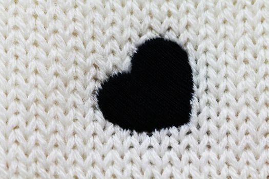 Knitted background of white color with black heart on it