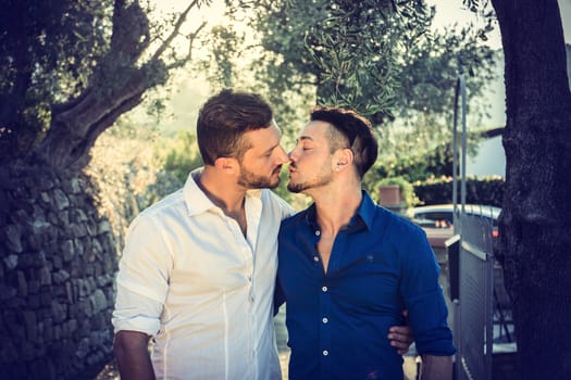 Stylish handsome men walking on sidewalk and kissing. Gay couple outdoor