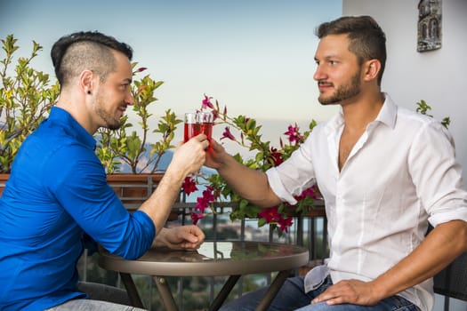 SIde view of two stylish handsome men sitting at the table with glasses of wine while looking face to face