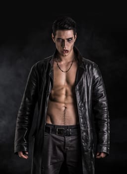 Portrait of a Young Vampire Man in an Open Black Leather Jacket, Showing his Chest and Abs, Looking at the Camera, on a Black Background.