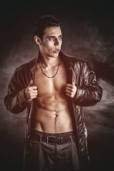 Portrait of a Young Vampire Man in an Open Black Leather Jacket, Showing his Chest and Abs, Looking at the Camera, on a Black Background.