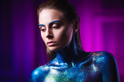 Portrait of an beautiful woman painted with purple cosmic colors and spangled. Body art project. Concept: fashion, makeup, extraordinary.