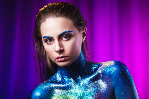 Portrait of an beautiful woman painted with purple cosmic colors and spangled. Body art project. Concept: fashion, makeup, extraordinary.