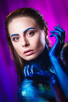 Portrait of an beautiful woman painted with purple cosmic colors and spangled. Body art project. Concept: fashion, makeup, extraordinary.