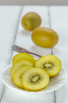 golden kiwi fruit and sliced on dish over white wooden background