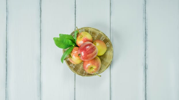 Top view red and yellow apple with leaves and  bamboo basket on  white wooden background with free space for text