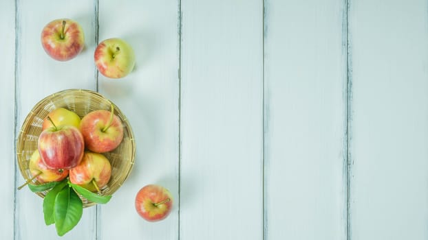 Top view red and yellow apple with leaves and  bamboo basket on  white wooden background with free space for text