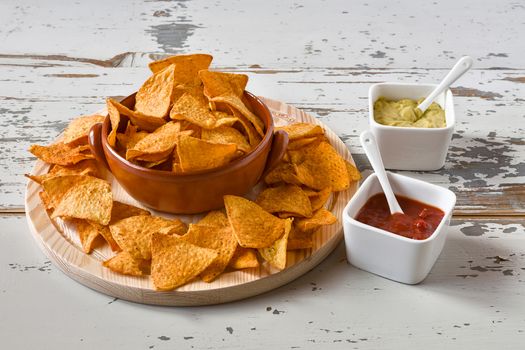 Nachos in an earthenware bowl over a chopping board and sauces