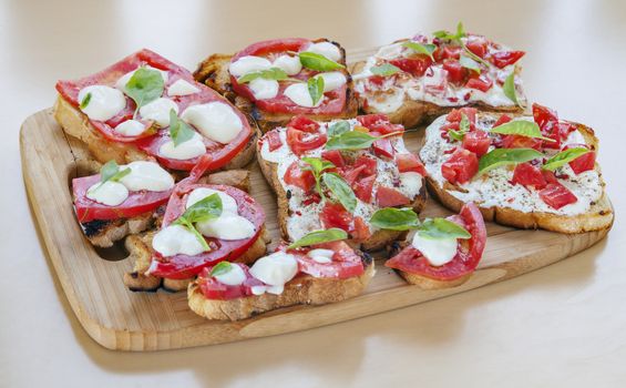 Creamy cheese over crispy toasts topped with tomatoes and basil. Horizontal image.