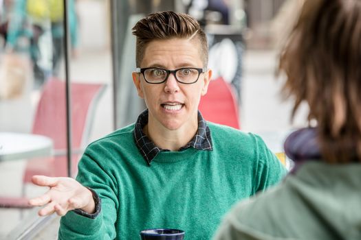 Excited woman in green shirt talking with unidentifiable friend at outdoor cafe