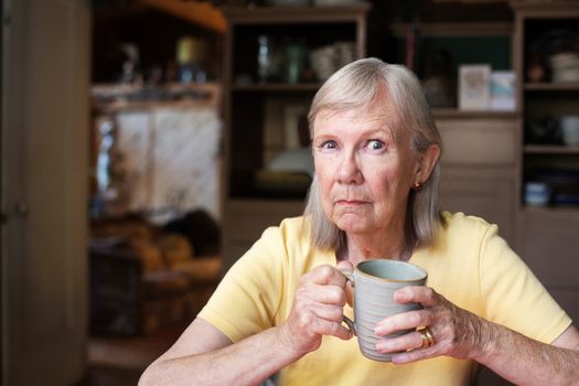 Single mature woman with angry expression holding cup while seated at table