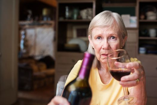 Older adult female offering a bottle of wine and glass sitting alone