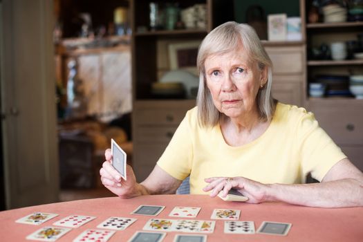 Woman in yellow shirt with serious expression and playing cards spread out