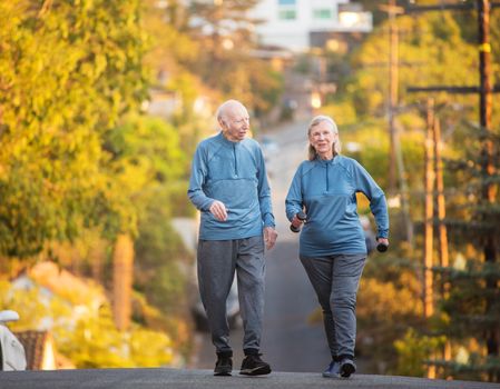 Enthusiastic man and woman with dumbbell weights walking up hill on street