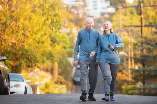 Laughing male and female senior couple walking along street with steep hill