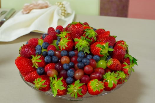 a fresh berries, blueberry, strawberry, raspberry in a glas bowl plate on a gray table
