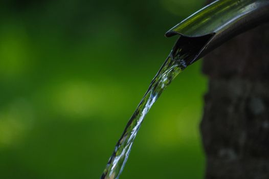 Close up of running water from a tap with green background