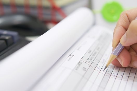 Hand with pencil over checklist form on desk at office.