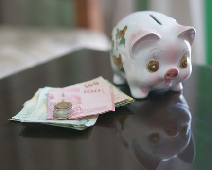 Lovely piggy bank with coins and banknote on wooden table.                               