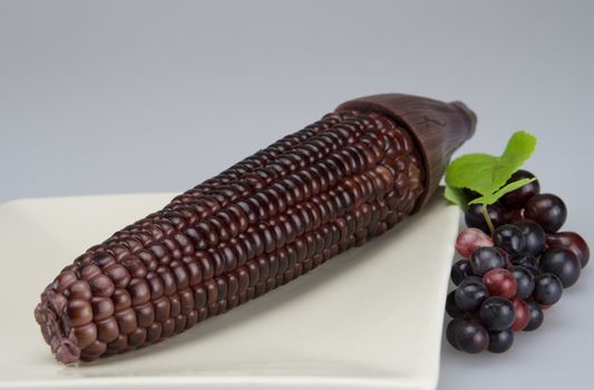 Purple corn put in plate and beside it has some grape.