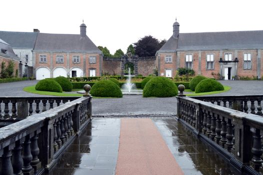 Court of castle with a water jet, bushes and a bridge.