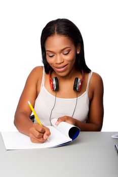 Cute beautiful happy smiling teenage student doing homework writing in notebook sitting at desk, on white.