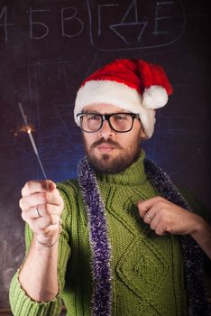 A young man with a beard in a green knitted sweater holding a Sparkler. The guy in glasses and a Santa hat welcomes the winter holidays. Old school