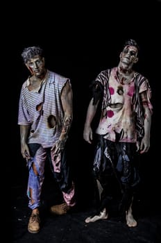 Two male zombies standing on black background walking towards camera