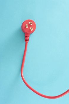 Red electrical lead with integrated three prong Australian plug on a blue background with copy space conceptual of power and energy