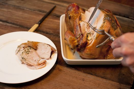 Man carving a delicious roast chicken placing slices of white breast meat on a plate on a wooden dining table