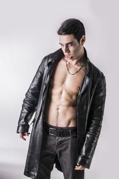 Portrait of a Young Vampire Man in an Open Black Leather Jacket, Showing his Chest and Abs, Looking at the Camera, on a Black Background.