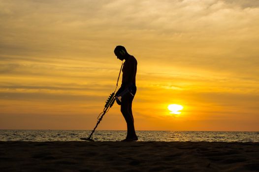 a treasure hunter with Metal detector on sunset on the beach