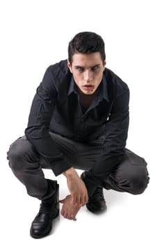 Portrait of a Young Vampire Man with Black Shirt Sitting on Floor with Hands Joined, Isolated on White