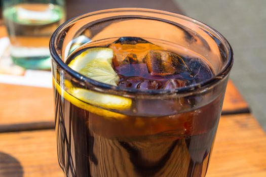 Detail, glass of cola with ice and lemon on a wooden table.