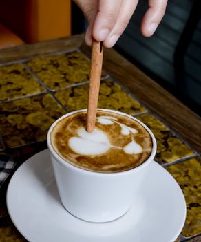 A coffee cup Latte being stirred by Cinnamon sticks.