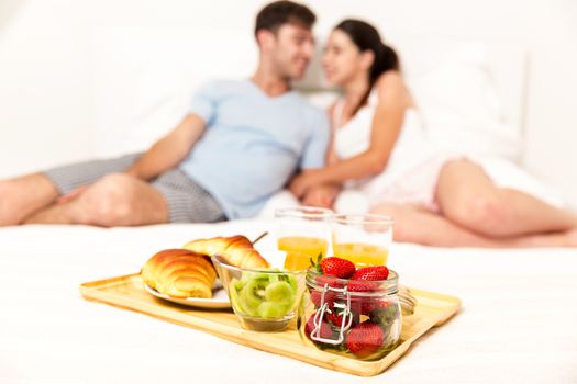 Young couple siting on the bed and ready to eat the breakfast