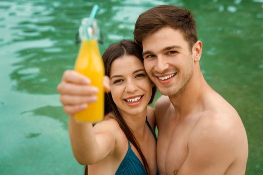 Young couple inside the pool and drinking natural juices