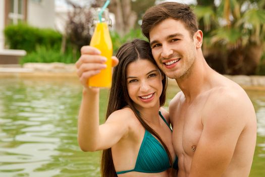 Young couple inside the pool and drinking natural juices