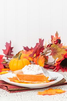 Slice of pumpkin pie plated among beautiful autumn colors.