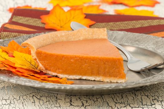 Slice of fresh baked pumpkin pie surrounded with colorful autumn leaves.