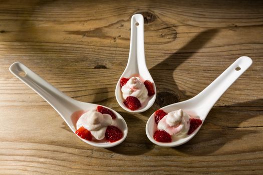 Mascarpone cream and strawberries on ceramic spoons over a wooden background