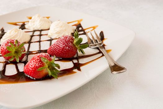 Strawberries with cream on a square plate with decorations and fork